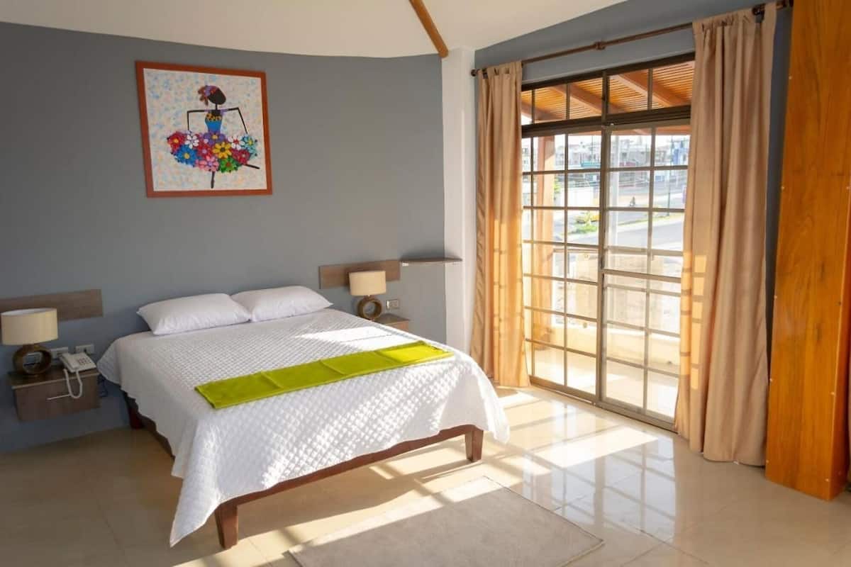 Habitació d'hotel amb un llit, dues taules de nit, una finestra amb cortines i un quadre a la paret.