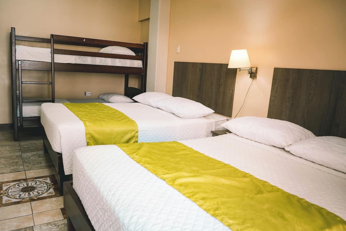 Habitació d'hotel amb dos llits, un llit superposat i una làmpada penjada a la paret.
