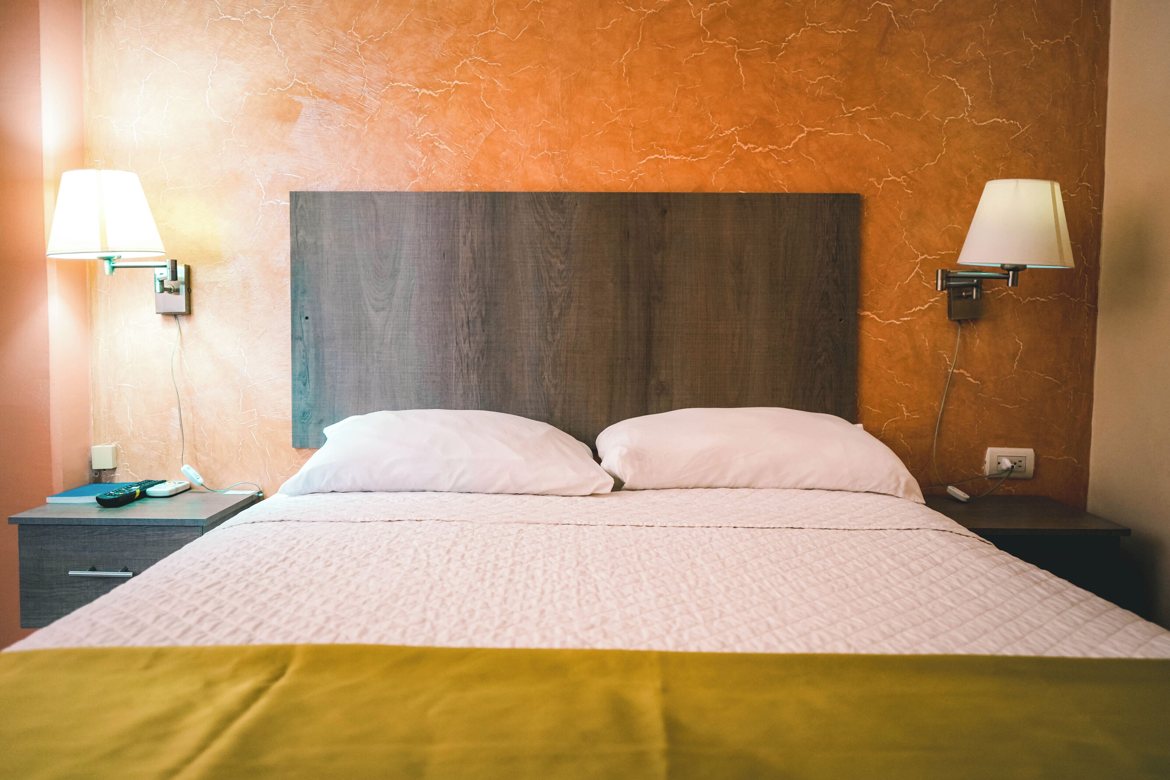 Une chambre d’hôtel avec un grand lit, deux tables de chevet et des lampes fixées au mur.