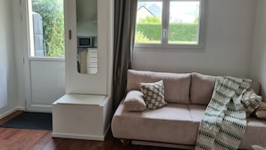 En moderne stue med sofa, et spejlskab og udsigt til en have gennem et vindue.