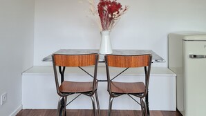 Et spiseområde med et hvidt bord, to stole, en vase med blomster og et fladskærms-tv på væggen.