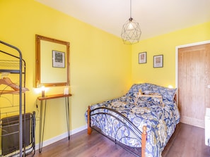 A bedroom with a bed, a bedside table with candles, a mirror, and a hanging light fixture.