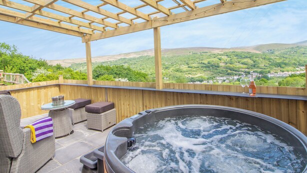 A hot tub with a wooden pergola, wicker furniture, and a view of a green valley. - 1 bedroom accommodation in Ammanford (Ammanford)
