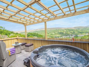 A hot tub with a wooden pergola, wicker furniture, and a view of a green valley.