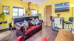 A modern living room with a leather sofa, a dining table, and a kitchen area with a window. - 1 bedroom accommodation in Ammanford (Ammanford)