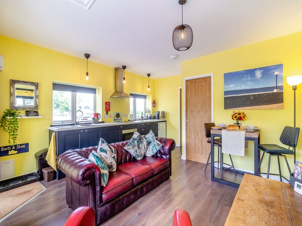 A modern living room with a leather sofa, a dining table, and a kitchen area with a window.