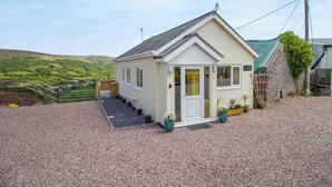 A small, single-story building with a sloped roof, a front porch, and a gravel driveway. - 1 bedroom accommodation in Ammanford (Ammanford)