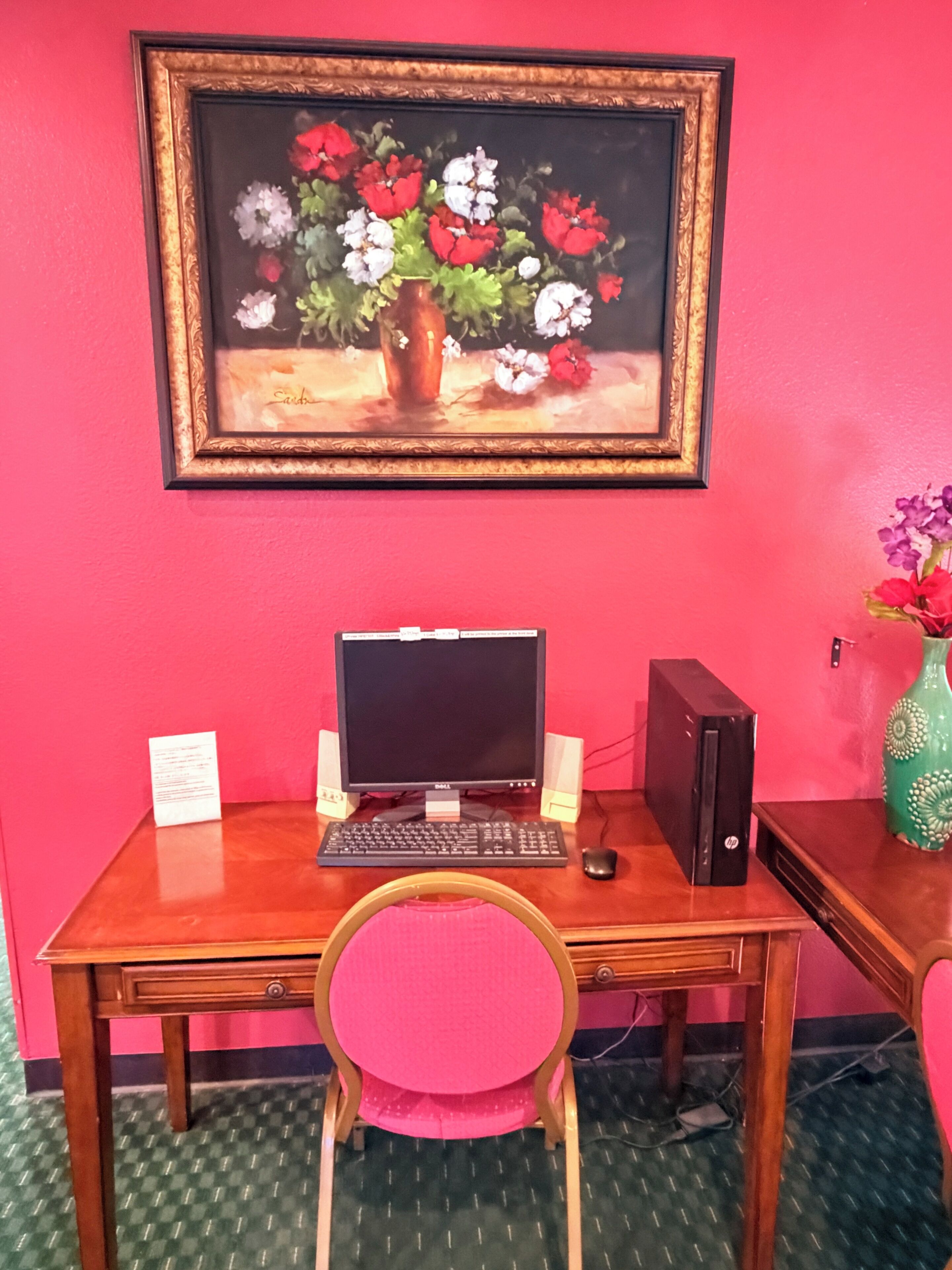 Un escritorio con una computadora, parlantes y una silla frente a un cuadro.