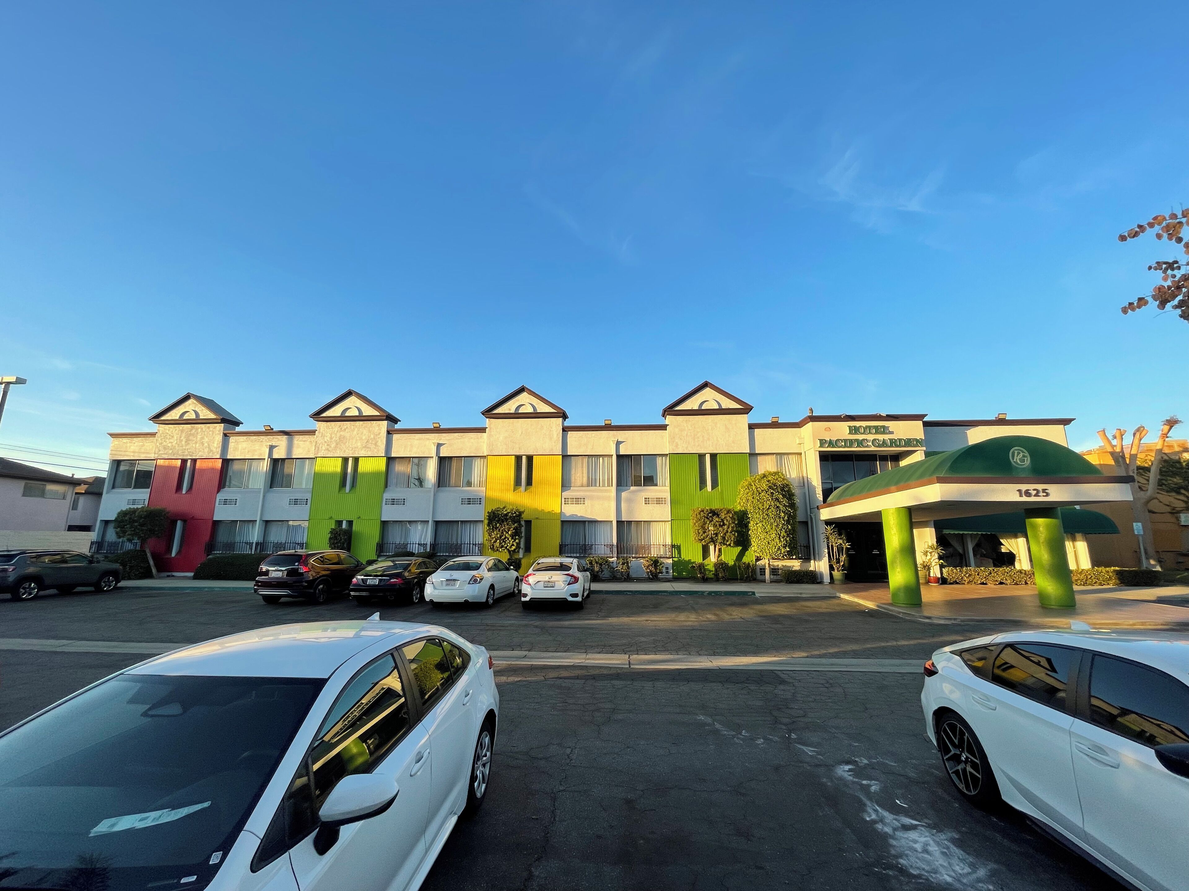 A hotel with a colorful facade, multiple parking spaces, and a clear blue sky.