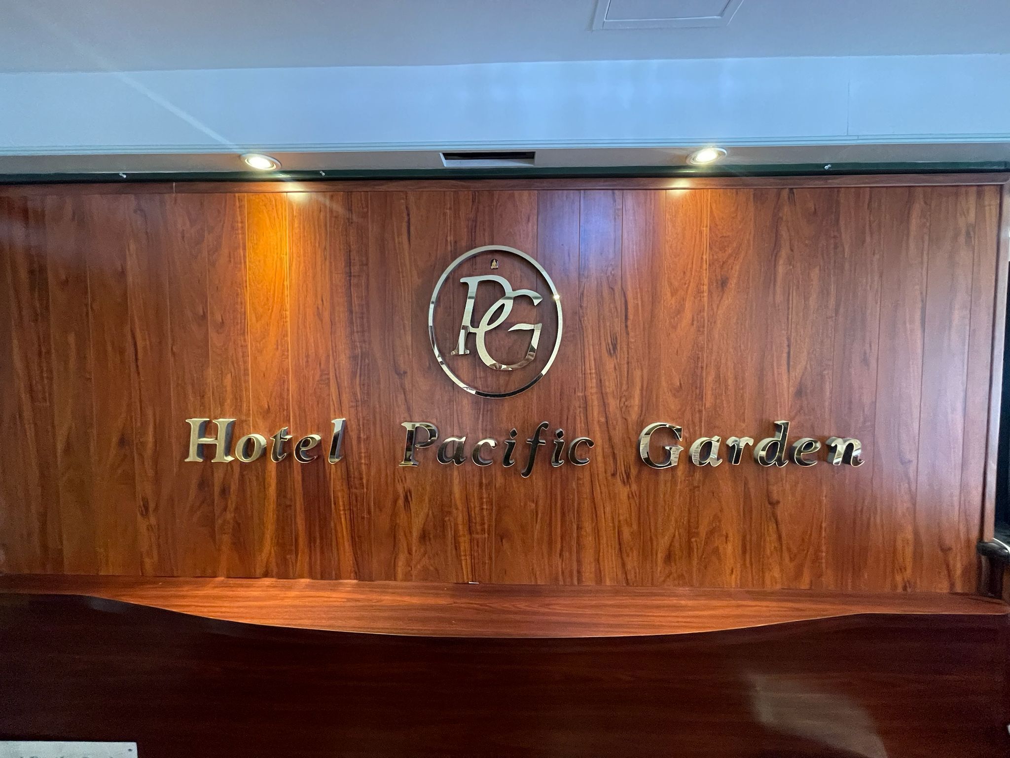 A wooden reception desk with the logo and name "Hotel Pacific Garden" engraved on it.