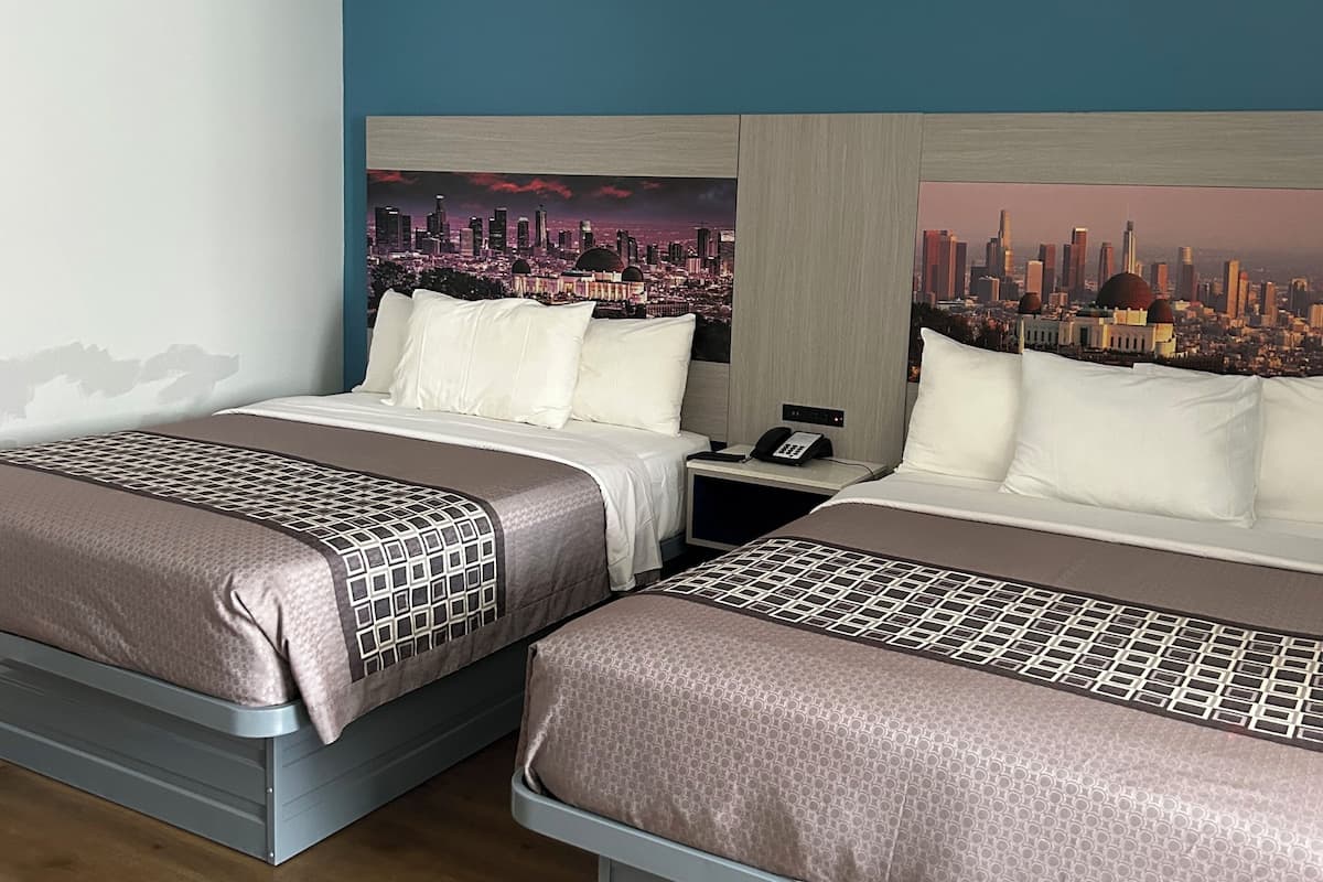 A hotel room with two beds, a cityscape mural on the wall, a phone on the nightstand, and a wooden floor.