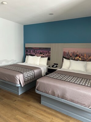 Une chambre d’hôtel avec deux lits, une fresque représentant un paysage urbain sur le mur, un téléphone sur la table de chevet et un plancher en bois.