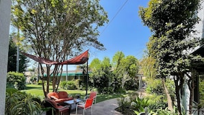 Un patio con mesa y sillas, rodeado de plantas en macetas y árboles.