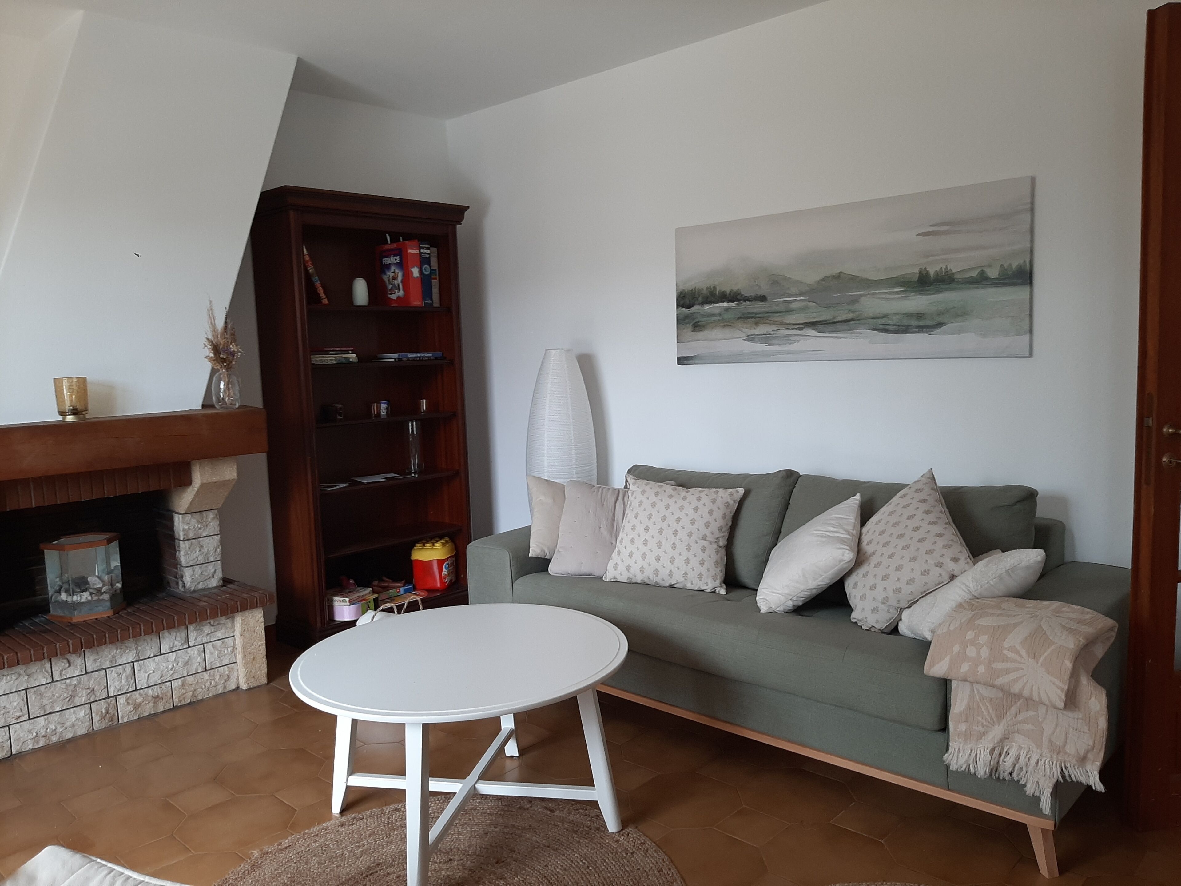 En hyggelig stue med pejs, en grøn sofa, et hvidt bord og en reol.