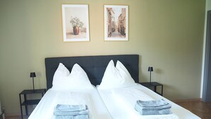A double bed with white linens and two pillows, flanked by nightstands with lamps, in a room with light green walls and two framed pictures.