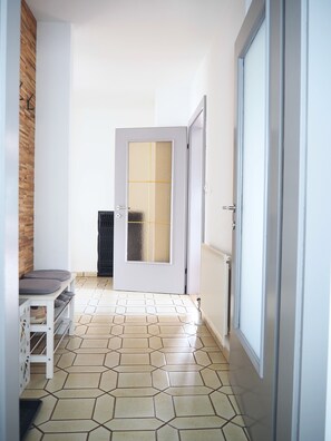 A hallway with a tiled floor, a bench, a door with frosted glass panels, and a radiator.