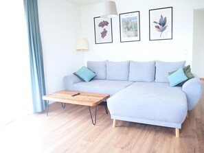Een moderne woonkamer met een lichtblauwe bank, een houten salontafel en drie ingekaderde kunstwerken aan de muur.