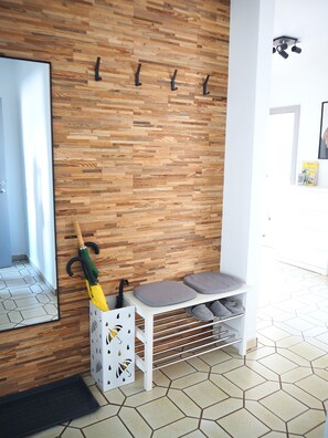 A room with a wooden wall, a white bench with cushions, a mirror, and a wall-mounted rack with hooks.