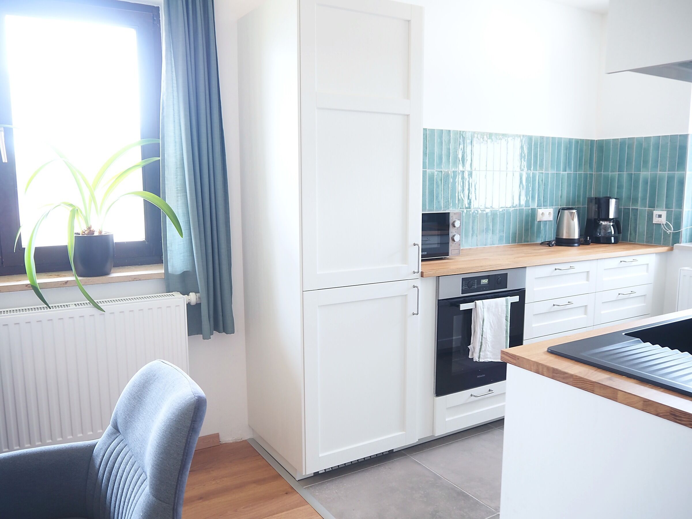 Una cocina moderna con armarios blancos, encimera de madera y una ventana con cortinas azules.