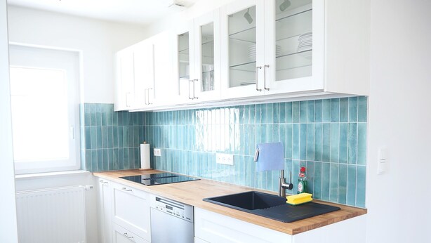 A modern kitchen with white cabinets, a black sink, and a blue-tiled backsplash.
