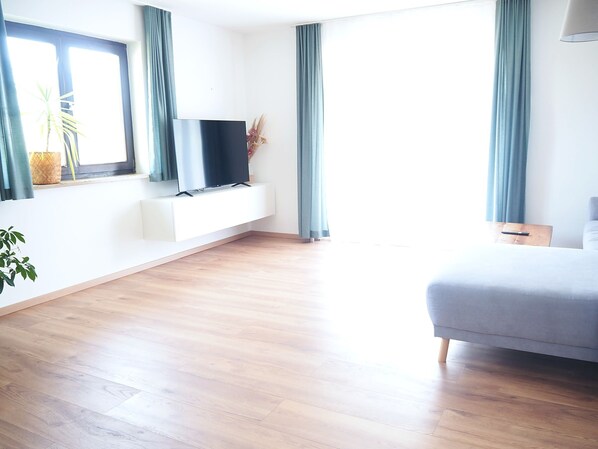 A modern hotel room with a flat-screen TV on a white console, a bed, and a window with curtains.