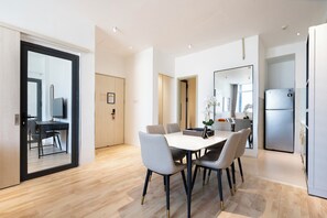 A modern kitchen with a dining area, wooden flooring, and a refrigerator. - THE ONE Saigon  By An Gia Hospitality (Ho Chi Minh City)