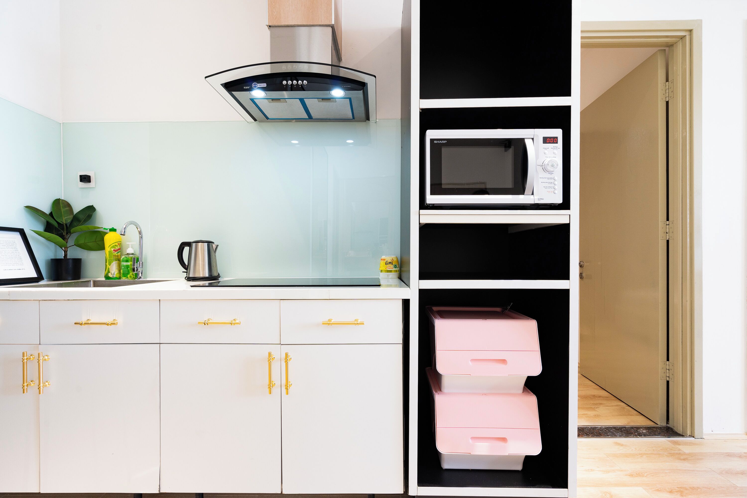 Una cocina moderna con armarios blancos, una campana extractora de acero inoxidable, un microondas y una planta.