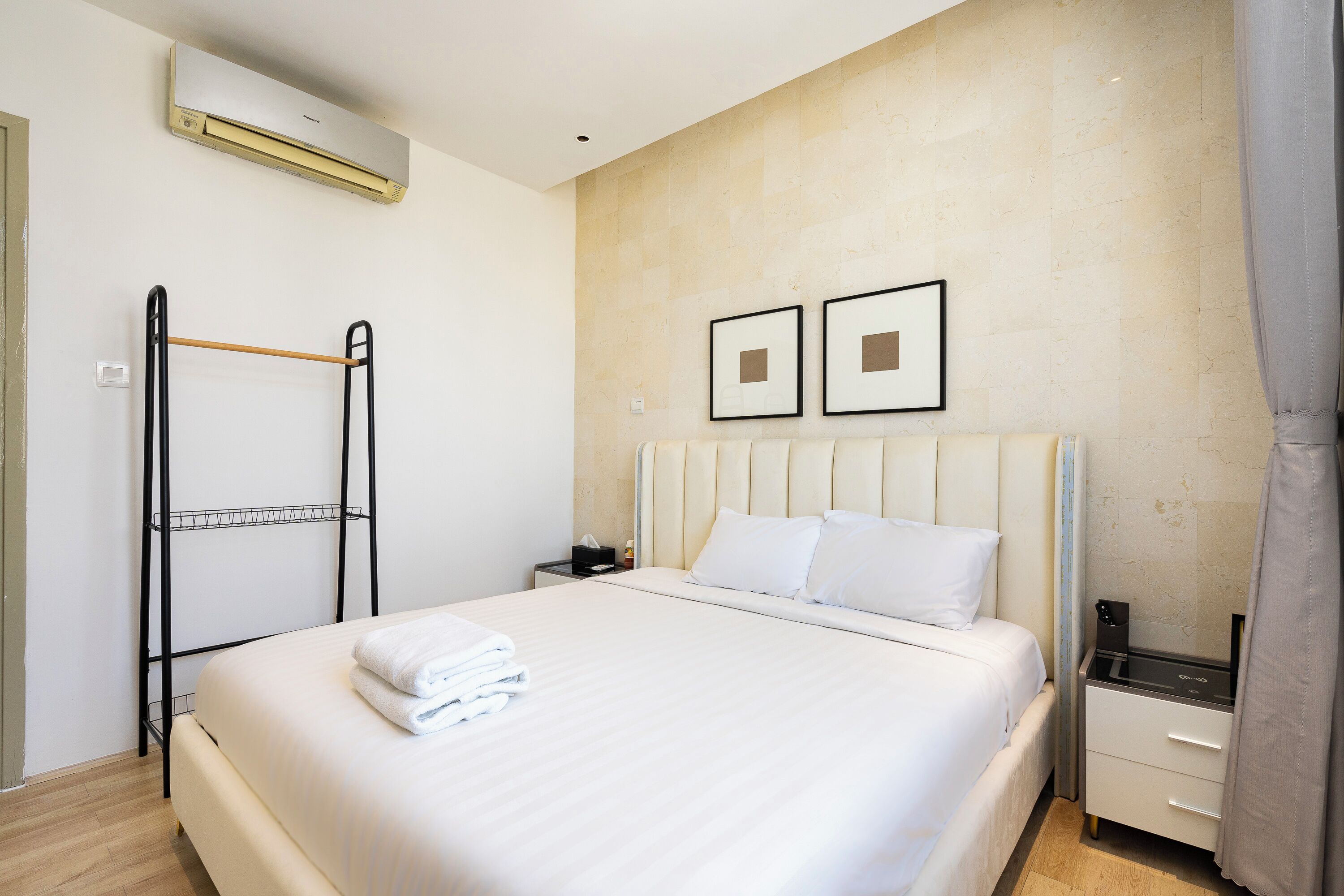 Een net opgemaakt bed met witte lakens, een nachtkastje met een lamp en een aan de muur bevestigde airconditioner.