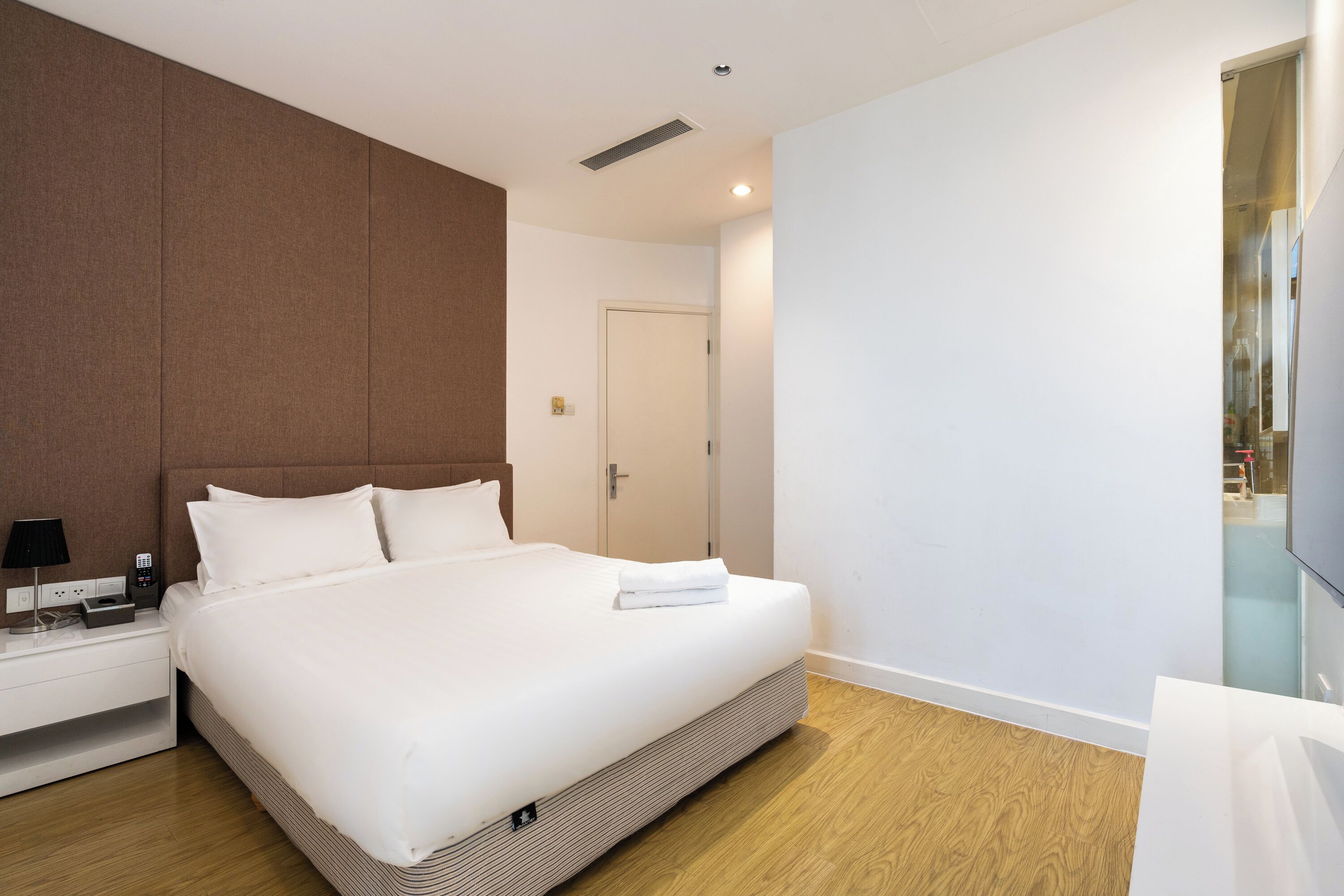 A modern hotel room with a large bed, a bedside table with a lamp, and a flat-screen TV mounted on the wall.
