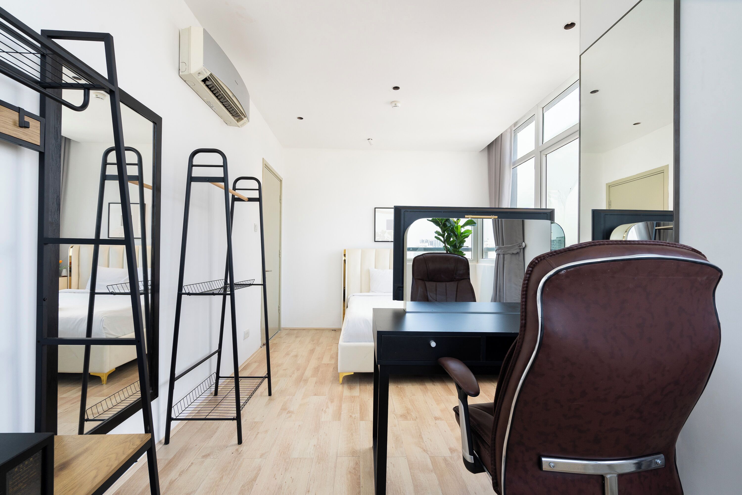 Moderni hotellihuone, jossa on työpöytä, tuoli ja suuri peili. Huoneessa on valkoisilla lakanoiden peitetyllä sängyllä ja ikkunasta tulee luonnonvaloa.