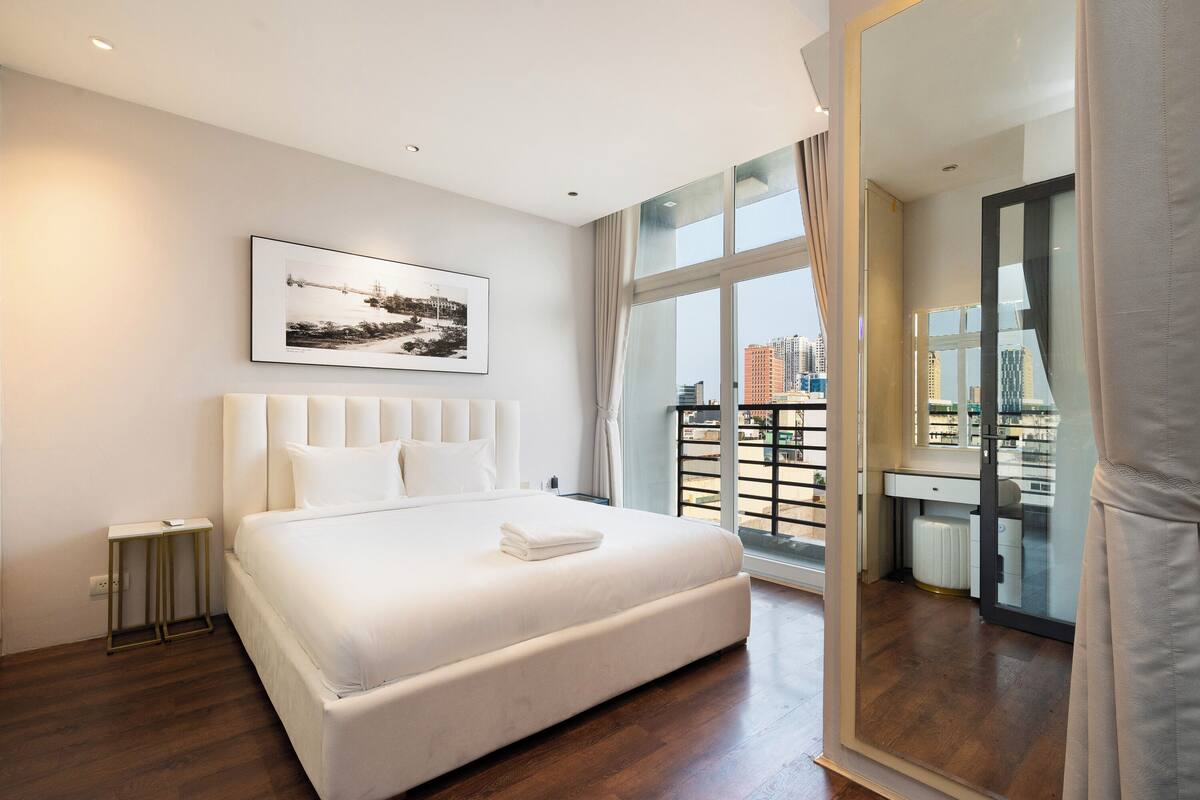 Une chambre d’hôtel moderne avec un grand lit, une vue sur la ville, un tableau encadré au mur et un grand miroir.