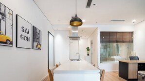 A modern kitchen with a central island, a dining area with chairs, and framed artwork on the wall. - THE ONE Saigon Luxury Citypoint By An Gia Hospitality (Ho Chi Minh City)