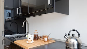 Une cuisine moderne équipée d’une bouilloire en acier inoxydable, d’une machine à café et d’une planche à découper en bois sur laquelle se trouvent des aliments.