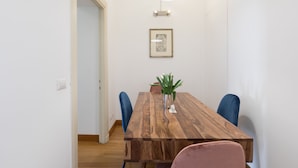 Un coin repas avec une table en bois, des chaises bleues et roses, une plante en pot et un tableau encadré au mur.