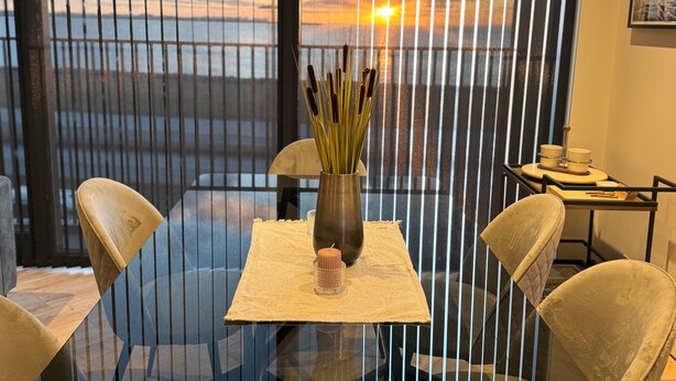 A modern dining area with a glass table, two chairs, a vase with reeds, and a candle. - Luxurious modern apartment in Reykjavik with ocean view! (Reykjavík)