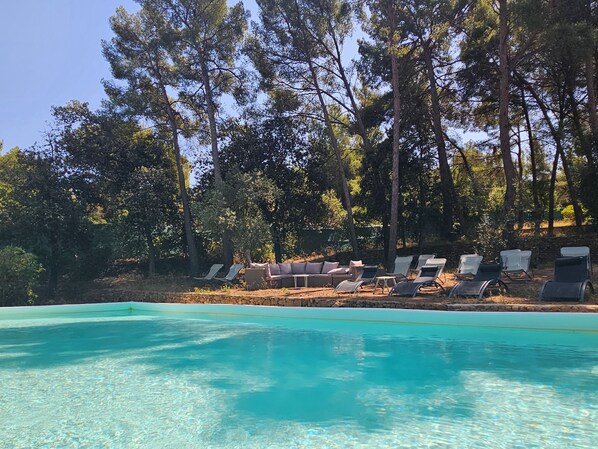 A clear swimming pool with lounge chairs and a stone wall.