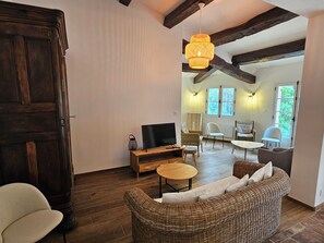 Ein gemütliches Wohnzimmer mit Fernseher, Korbmöbeln und einer Holzbalkendecke.