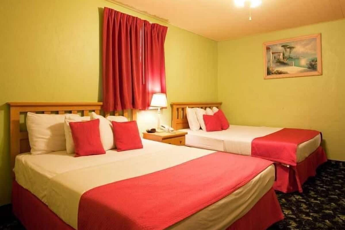 A hotel room with two beds, each with red bedding and pillows, a nightstand with a lamp, and a painting on the wall.