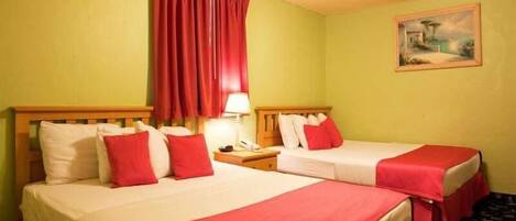 Een hotelkamer met twee bedden, elk voorzien van rode beddengoed en kussens, een nachtkastje met een lamp, en een schilderij aan de muur.