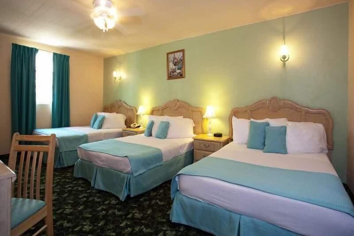 A hotel room with two single beds, a wooden chair, a desk, and a ceiling fan.