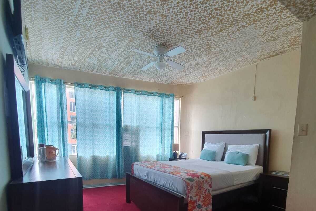 A bedroom with a bed, a desk, a ceiling fan, and a window with curtains.