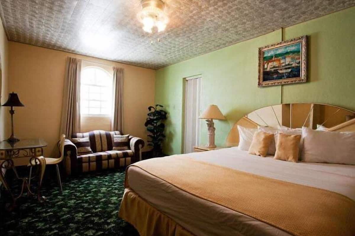 A hotel room with a large bed, a chair, a table, and a painting on the wall.