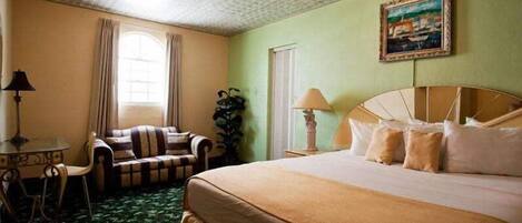 A hotel room with a large bed, a chair, a table, and a painting on the wall.