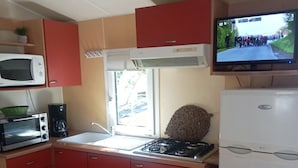 Una cocina compacta con armarios rojos, un refrigerador blanco, una estufa, un microondas y un televisor montado sobre la estufa.