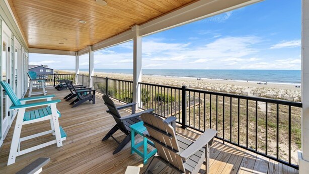 A covered deck with wooden flooring, outdoor seating, and a view of the beach. - New luxury ocean front w/Heated private pool, Elevator, 8 Bed/8 Bath (Holden Beach)