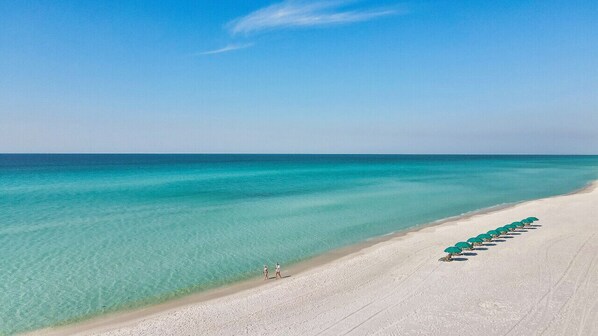 Une plage à l’eau turquoise et limpide, bordée d’une rangée de parasols verts.