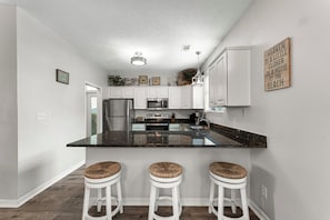 A modern kitchen with white cabinets, a granite countertop, and three stools with woven seats.