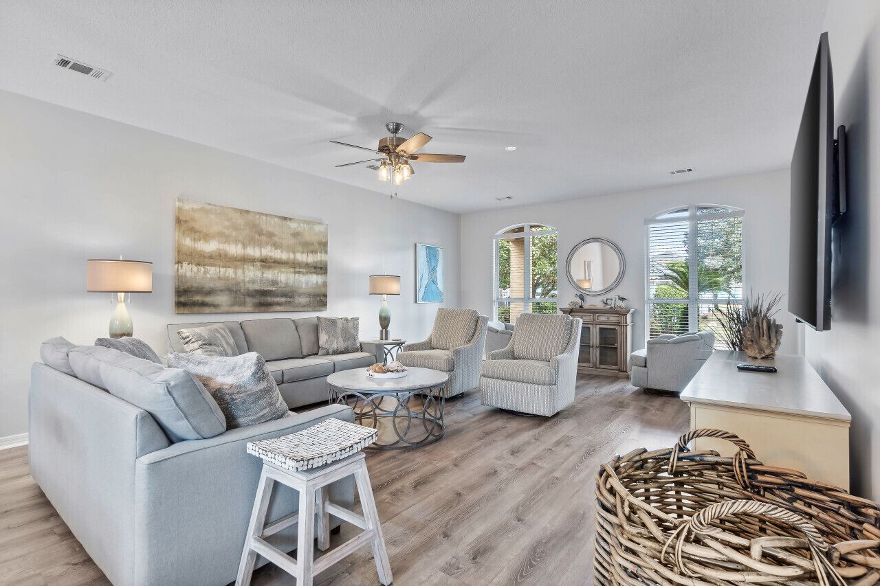 A spacious living room with a grey sofa, two armchairs, a coffee table, and a ceiling fan.