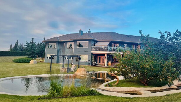 A two-story house with a large front yard, a pond, and a well-maintained garden. - Charming Guest House with Beautiful Mountain View & Spa....Pet Friendly (De Winton)