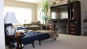 A living room with a sofa, a television, a fireplace, and a large plant. - Charming Guest House with Beautiful Mountain View & Spa....Pet Friendly (De Winton)